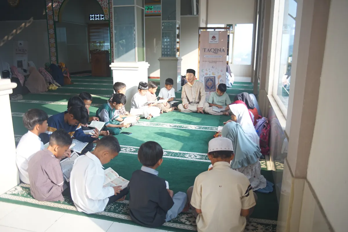 Sejumlah anak duduk melingkar di atas karpet hijau, mengikuti kegiatan belajar Al-Qur'an bersama pengajar